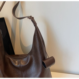 Detail of a dark brown vintage hobo bag featuring a knotted shoulder strap and pendant