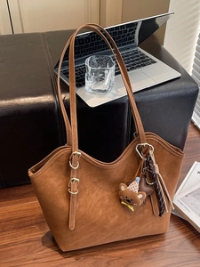 Brown suede tote bag with bear charm and long straps in a cozy office setting