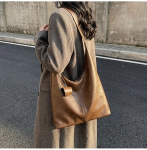 Detail of vintage brown leather hobo bag with textured surface and small round charm