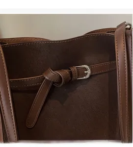 Macro detail of dark brown suede tote bag featuring a belt buckle and fine stitching