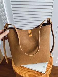 Sac seau en cuir marron minimaliste avec fermoir doré et bandoulière large sur tabouret