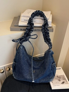 Retro washed denim shoulder bag with pleated strap and bow details on white desk