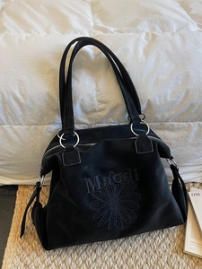 Grand sac cabas noir avec broderie marguerite et inscription Maiodi sur un lit