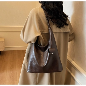 Detail view of large dark brown tote bag with pebble leather texture on model's shoulder