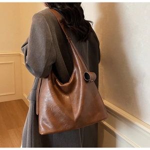 Detail view of large brown leather tote bag showing textured vertical stitching and side buckle