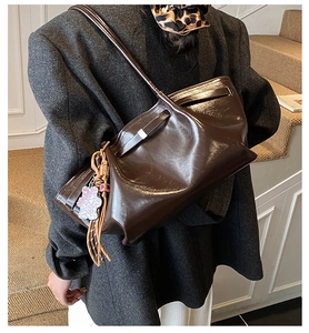 Detail of dark brown leather tote bag with leopard bear charm and tassel on grey blazer
