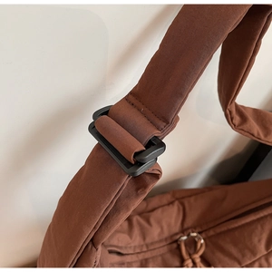 Detail of adjustable black matte strap buckle on brown padded nylon shoulder bag