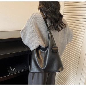 Close-up of minimalist black matte leather hobo bag worn by model in a modern room
