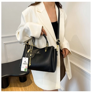 Détail du sac à bandoulière noir avec doubles poignées, ferrures dorées et breloque cœur