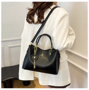 Détail du sac à main en cuir noir avec poignée dorée, logo kangourou et breloque cœur