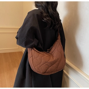 Detail of dark brown quilted crescent bag showing wavy stitching and side logo tag