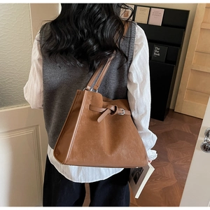 Vue détaillée d'un sac cabas vintage marron foncé porté par un mannequin dans une bibliothèque