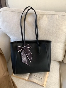 Classic black pebbled leather tote bag with a patterned scarf on a neutral sofa