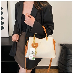 Détail d'un sac à main bicolore crème et caramel avec logo doré et pendentif cœur