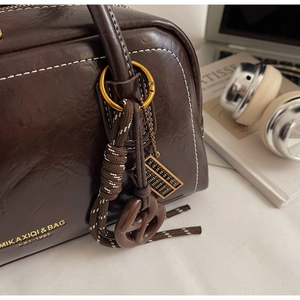 Détail du sac en cuir ciré marron foncé avec coutures contrastées et breloques vintage
