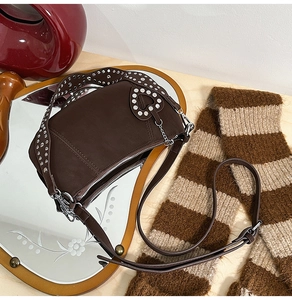 Detail of silver rivets on brown leather shoulder strap with a heart-shaped tag charm