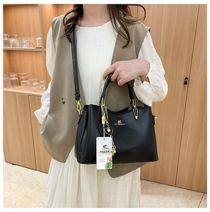 Détail du sac bandoulière noir avec finitions dorées et breloque cœur à pompon