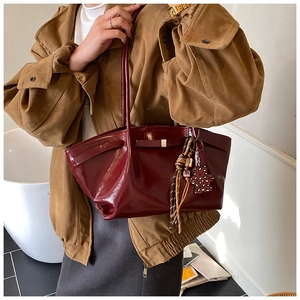 Detail of dark red patent leather tote bag with leopard bear charm and woven straps