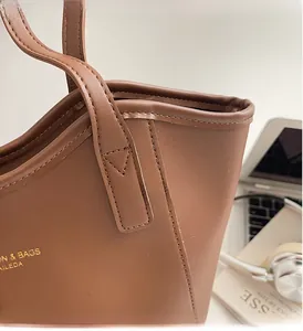 Detail of premium brown leather tote bag showing handle stitching and gold brand logo