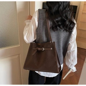 Sac cabas en cuir marron foncé avec boucle métallique porté par un mannequin en intérieur