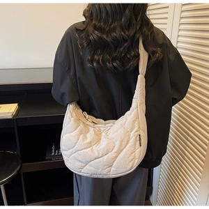 Detail of light beige quilted crescent bag featuring wave stitching and wide shoulder strap