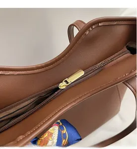 Detail view of the smooth golden zipper closure on a large brown leather tote bag