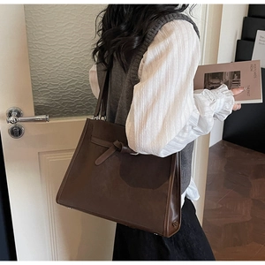 Détail d'un sac cabas vintage marron foncé avec nœud porté à l'épaule par un mannequin
