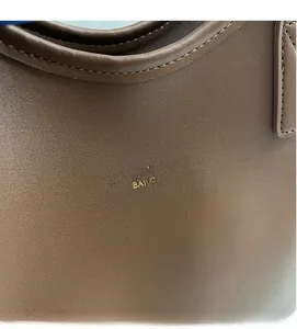 Detail shot of brown leather tote bag with fine stitching and golden logo engraving