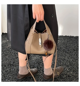 Detail of khaki pebbled leather bucket bag with silver clasp and faux fur charm