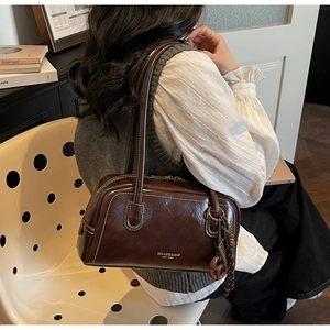 Détail du sac boston marron foncé avec surpiq surpiqûres blanches et pendentif à pompon