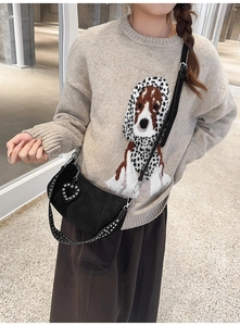 Detail of black suede dumpling bag with silver rivets and heart charm on a beige sweater