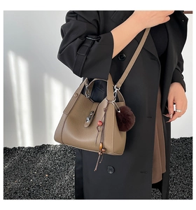 Detail of tan pebble leather bucket bag featuring metal lock and brown pompom charm