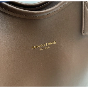 Close-up of brown matte leather tote with gold foil stamped logo and fine stitching details