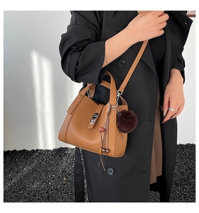 Brown litchi grain bucket bag with plush ball charm and tassel on a stylish model