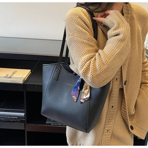 Detail of black leather tote bag with elegant floral scarf and golden logo lettering