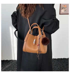Detailed view of brown bucket bag with pompom charm on a model in wool coat
