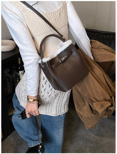 Detail of a brown lychee leather bucket bag with white faux fur trim and metal buckle