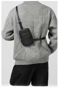 Close-up of black litchi grain leather crossbody bag with adjustable strap on gray sweater