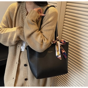 Close-up of black leather tote bag with a decorative silk scarf and golden logo details