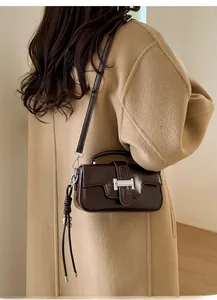 Detail of a dark brown glossy crossbody bag featuring a silver H-shaped clasp on a model