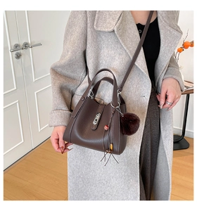 Detail view of dark brown litchi grain bucket bag with fur ball charm on grey coat