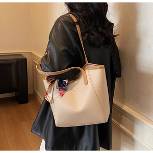 Detail of a large beige tote bag with brown straps and a decorative silk scarf accessory
