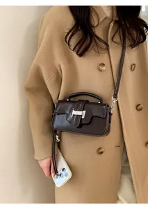 Close-up of a vintage brown leather handbag with silver metal buckle on camel coat