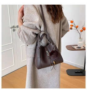 Detail of dark brown lychee leather handbag with metal buckle and soft fur ball charm