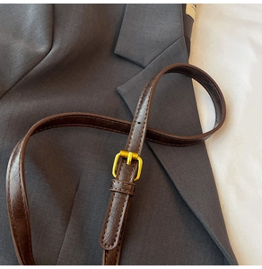 Gros plan d'une ceinture vintage en cuir marron avec boucle dorée sur un blazer gris chic