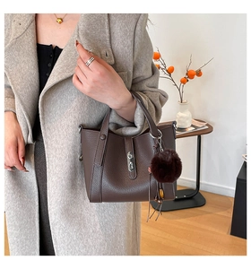 Close-up of deep brown litchi pattern leather handbag with metal lock and fur ball charm