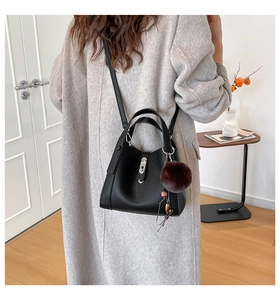 Detail view of black litchi grain bucket bag with plush charm on a grey wool coat