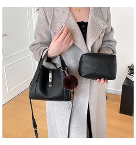 Detail of black lychee grain leather bucket bag set with silver hardware and fur pompom
