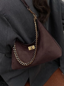 Sac hobo marron en daim avec chaîne dorée porté sur un costume gris minimaliste