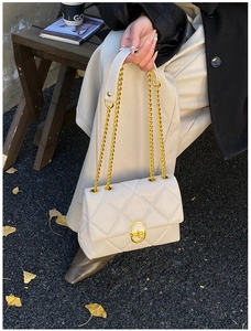 Detail of quilted beige crossbody bag with gold chain strap on autumn park bench
